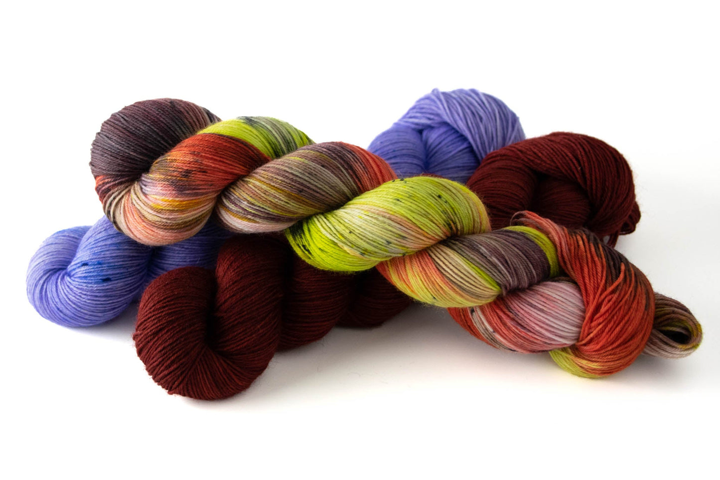 A skein of the Sea Slug colorway laying over skeins of Nudibranch (a deep red) and Dorid (a neon lilac).