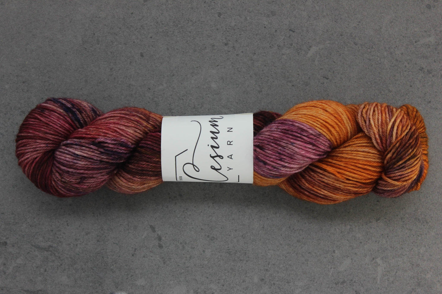 A skein of hand-dyed wool yarn with sections of orange and maroon.