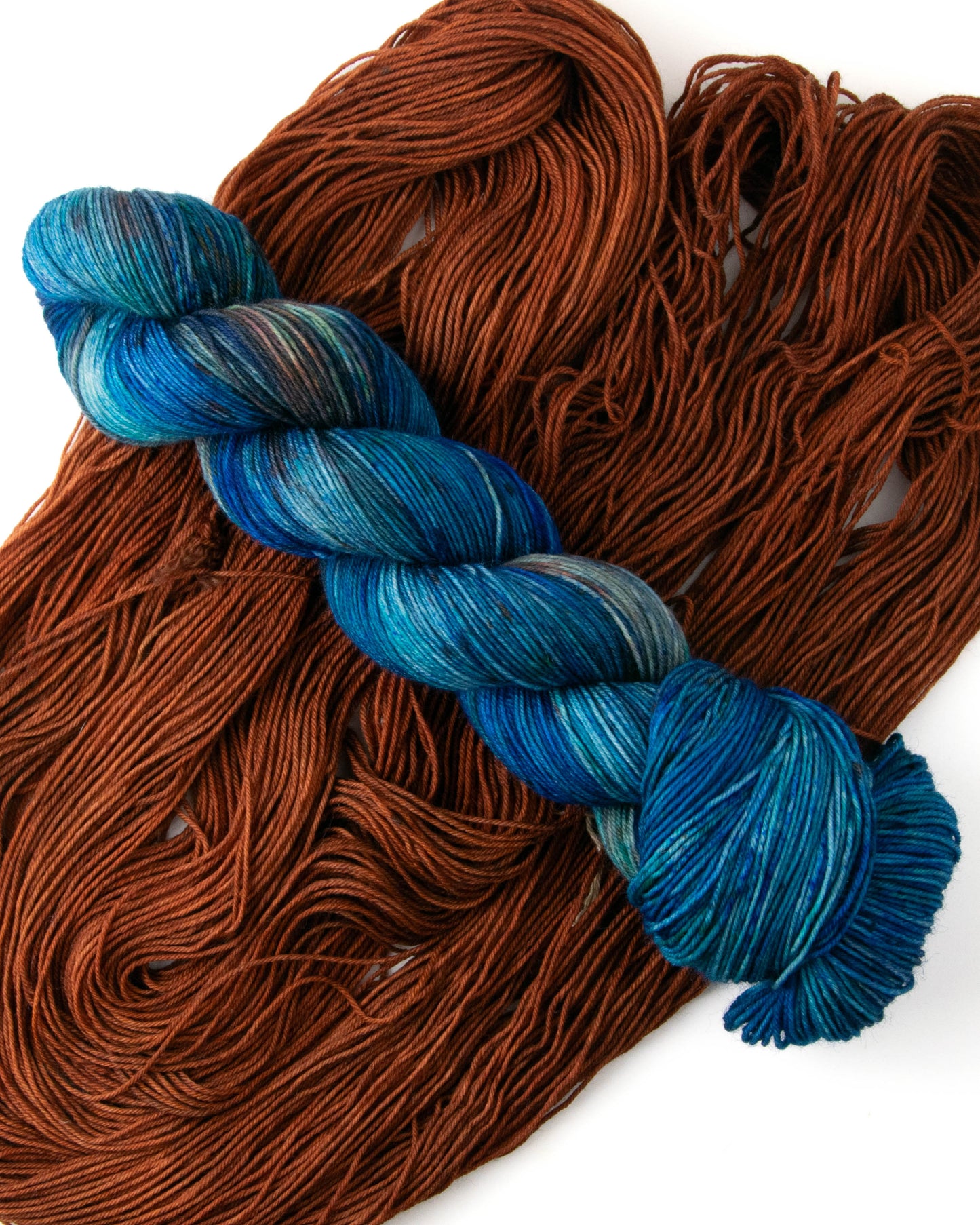 A moody blue skein of yarn with orange speckles on an almost brown orange pile of yarn.