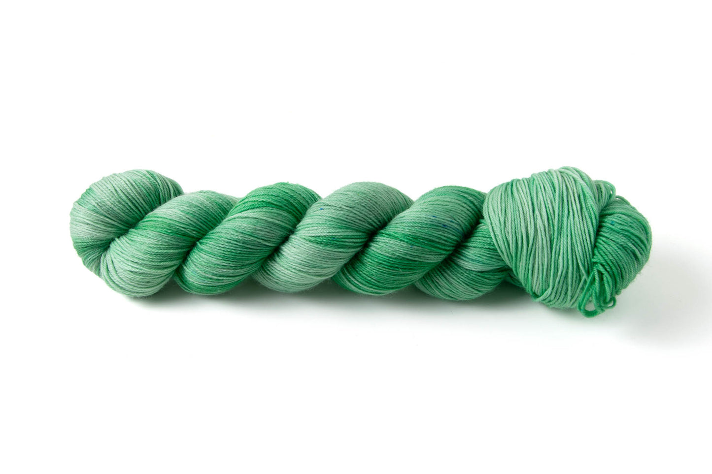 A skein of mint green hand-dyed yarn with tiny blue micro-speckles.