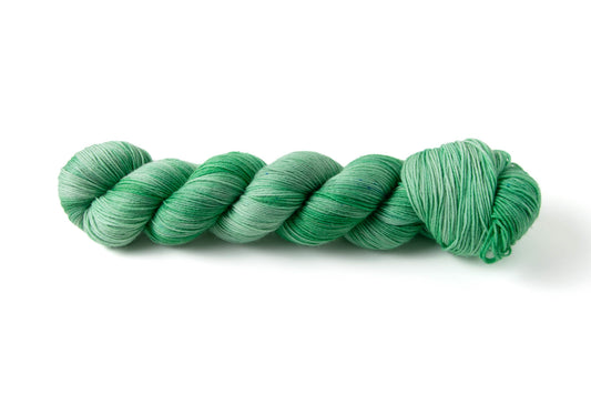 A skein of mint green hand-dyed yarn with tiny blue micro-speckles.