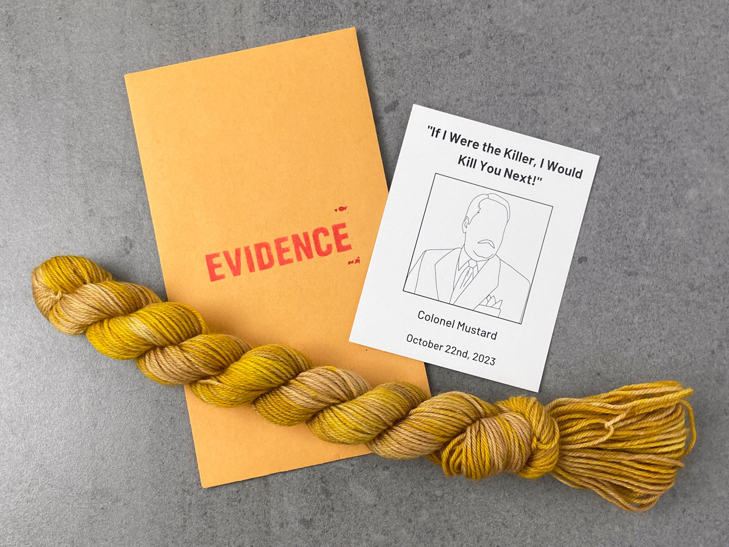 A skein of mustard yellow yarn on top of an envelope stamped with "Evidence" and a card with a drawing of Colonel Mustard on it.