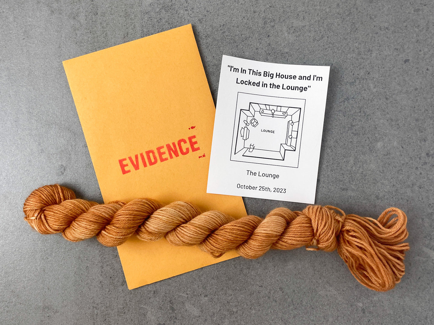 A skein of muted orange tonal yarn on top of an envelope stamped with "Evidence" and a card with an overhead drawing of the lounge on it.