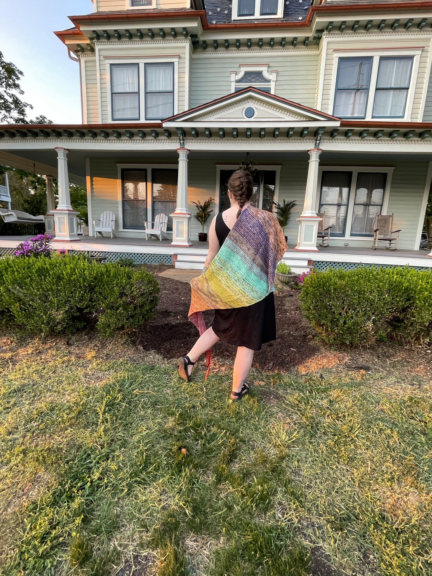 Cat stands in front of a mansion with a rainbow shawl spread across her back.