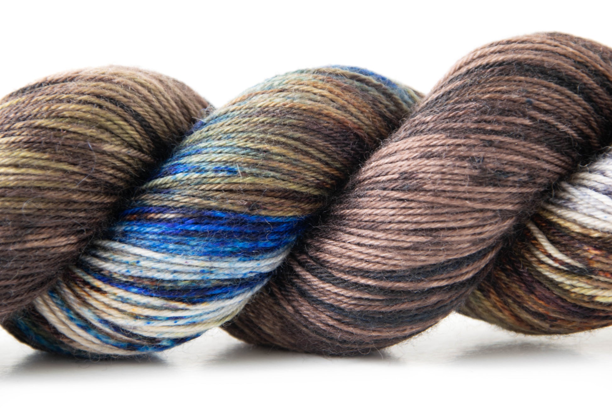Close view of the variegation of the yarn, including large swaths of blue, a sandy brown background, and dark brown speckles.