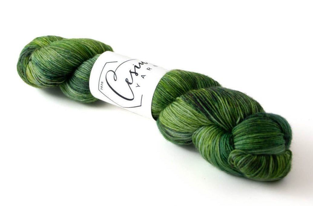 A skein of variegated hand-dyed wool yarn comprised of many shades of green.