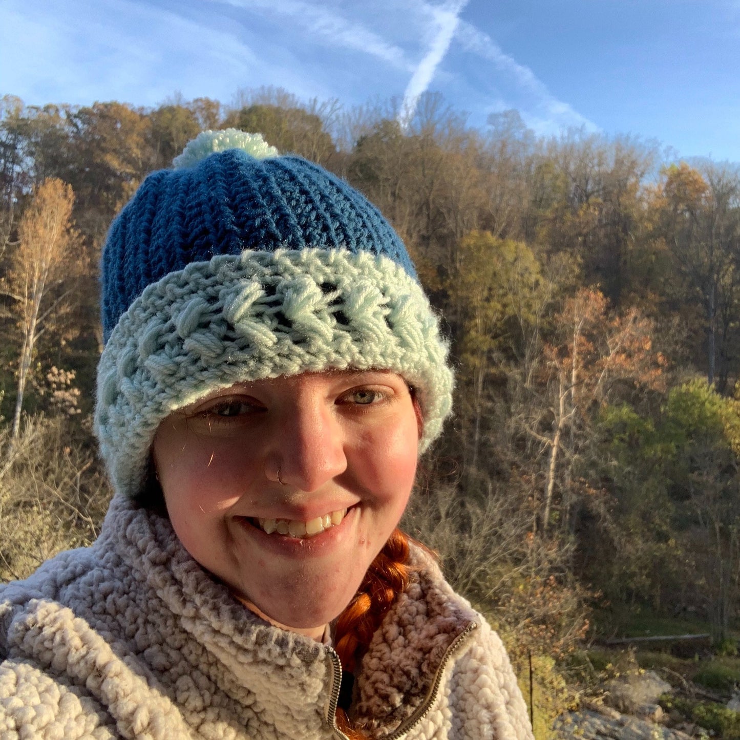 Cat smiles at the camera wearing a hat made of teal and aqua acrylic yarn.