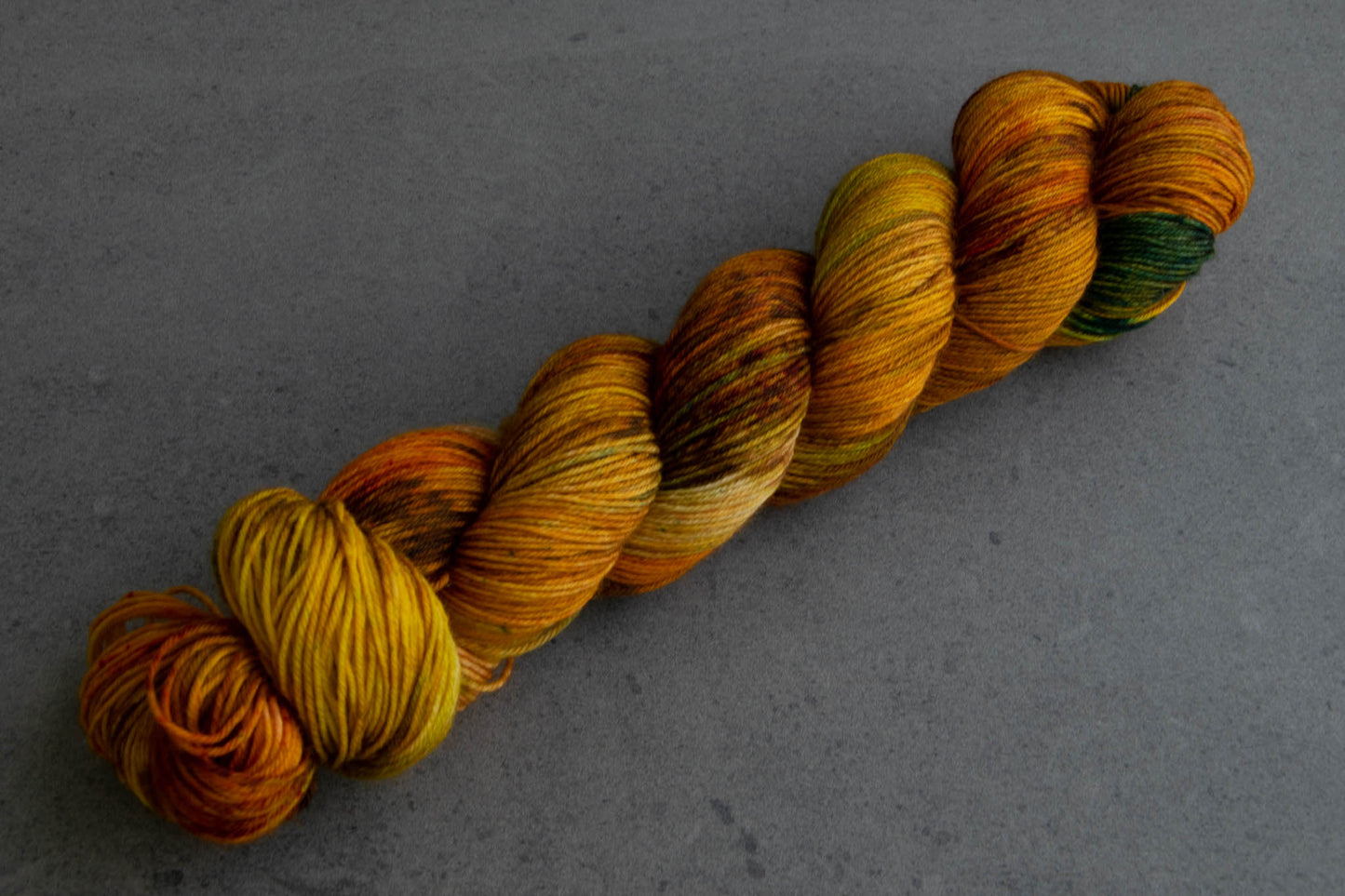 A skein of warm brown, yellow, orange, and green hand-dyed wool yarn.