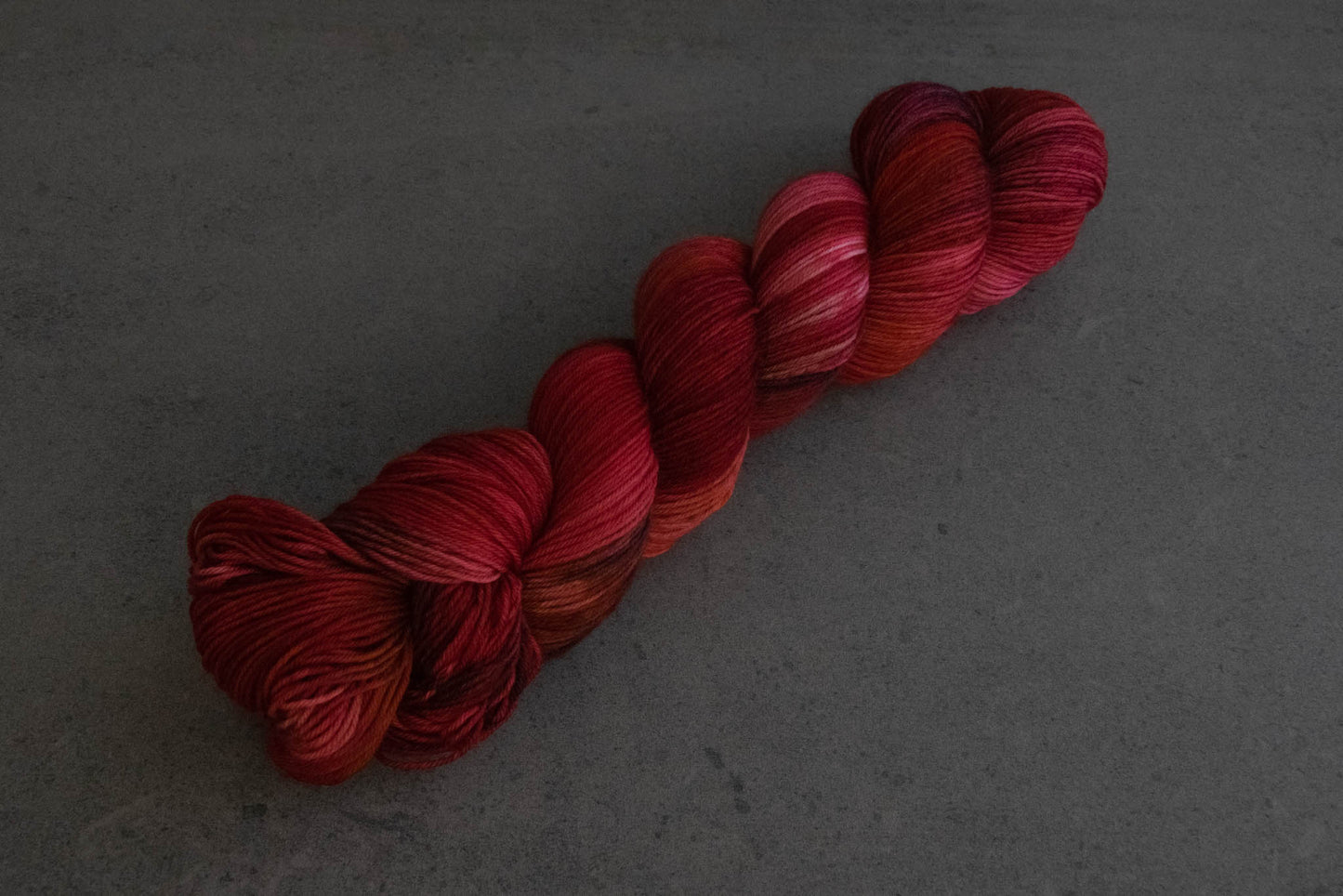A saturated skein of red variegated hand-dyed yarn with sections of pink and plum.