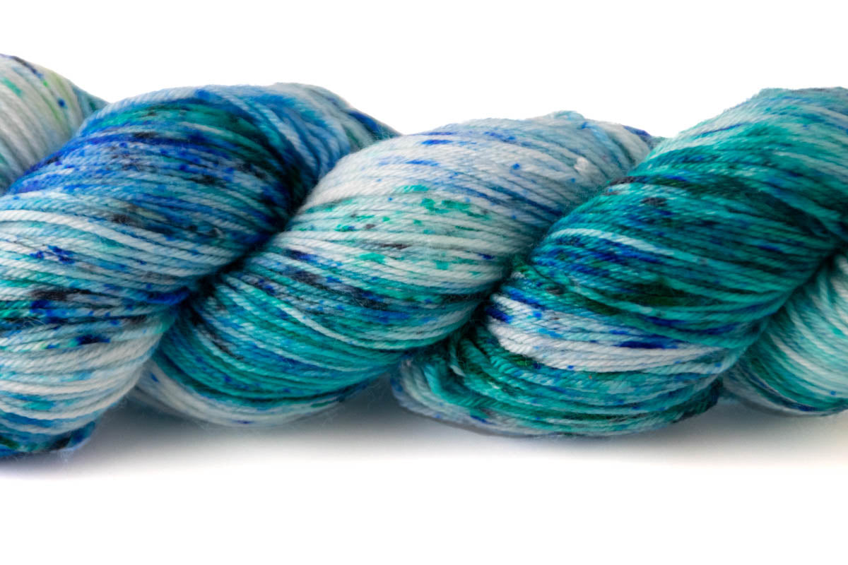 Closeup (but slightly blurry) view of the variegated quality of the yarn, with dark blue to navy speckles.