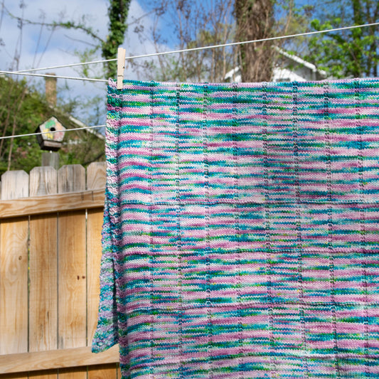 A blanket hanging on a clothesline with a pattern of squares and rectangles and a seed-stitch border.