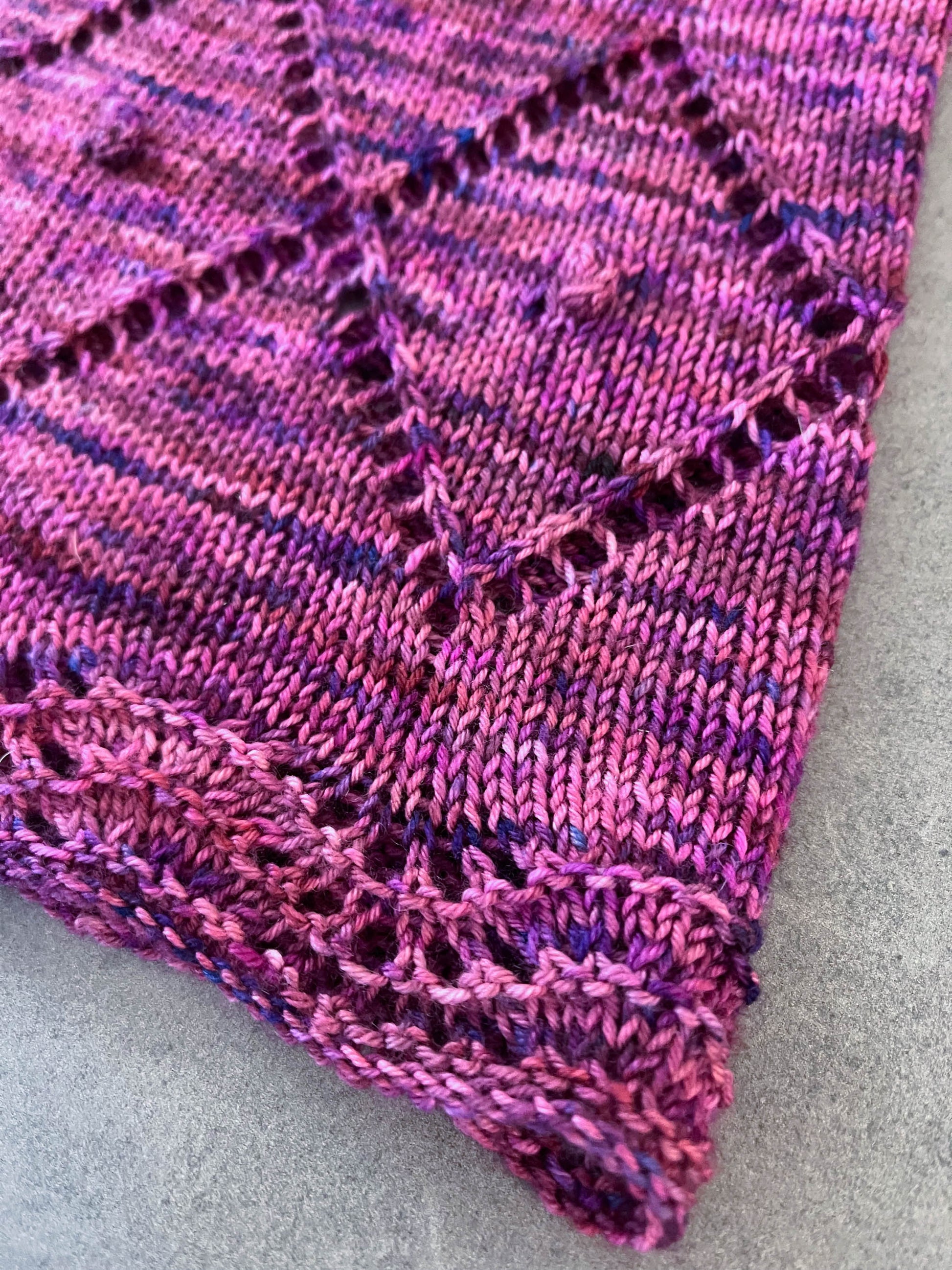 A corner view of a knit cowl with a wave border, lace zig-zag pattern, and popcorn stitch accents.