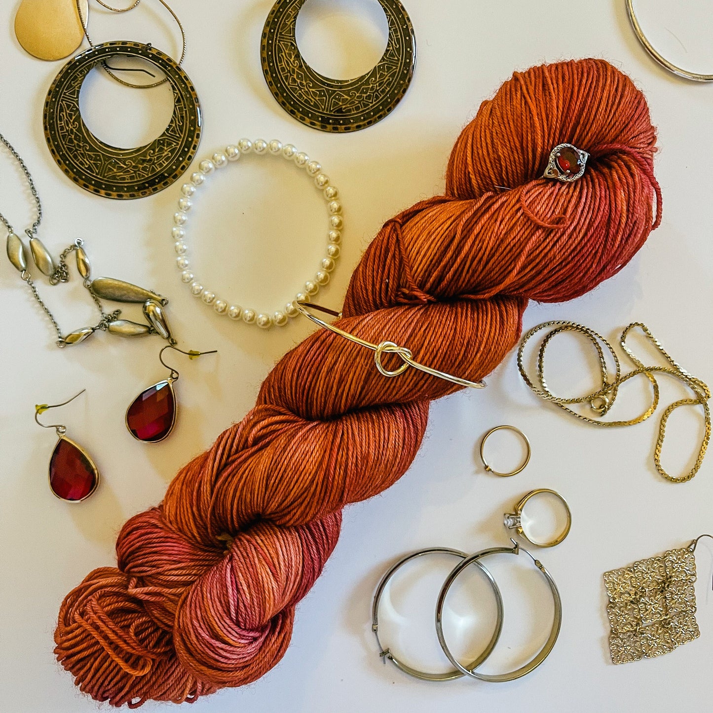 A red skein of hand-dyed merino yarn with gold and ruby jewelry around it