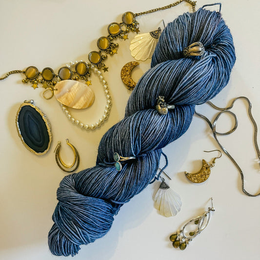 A skein of Hey Ewe Guys hand-dyed yarn surrounded by jewelry.