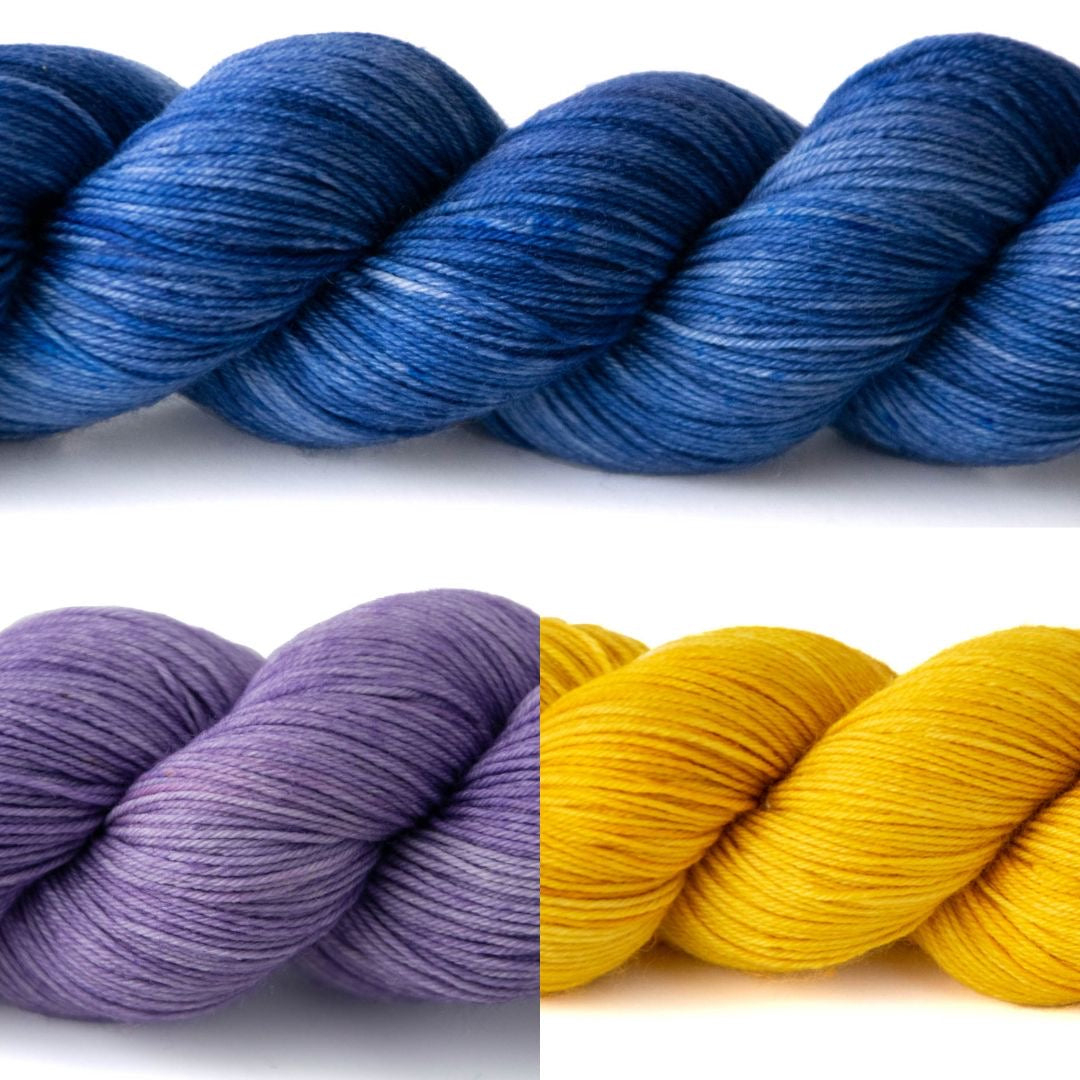 A large skein of navy blue yarn on top of one purple and one yellow skein.