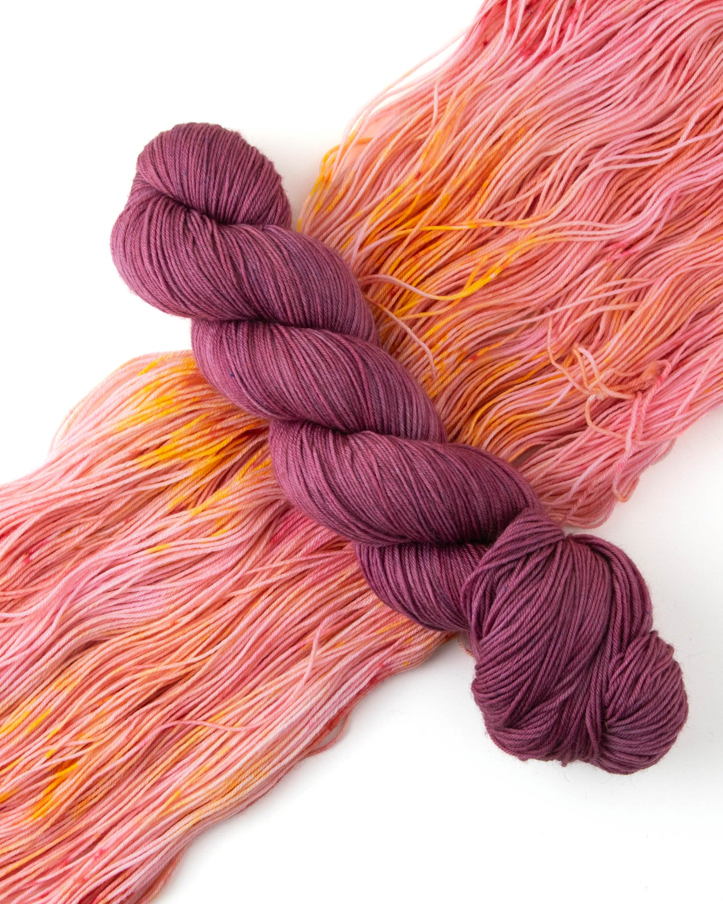 A skein of magenta yarn on top of pink and orange yarn.