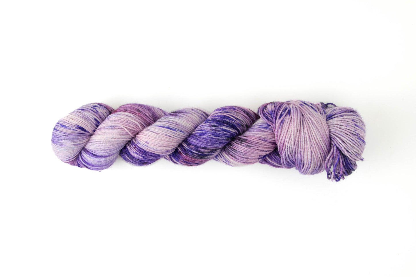 A skein of yarn with many shades of purple on it, including a deep grape, a soft pastel, and a pinky magenta.