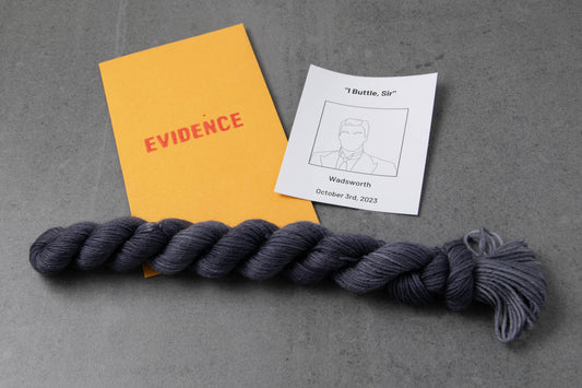 A dark gray mini skein on an envelope stamped with "Evidence" and a card with a drawing of Wadsworth.