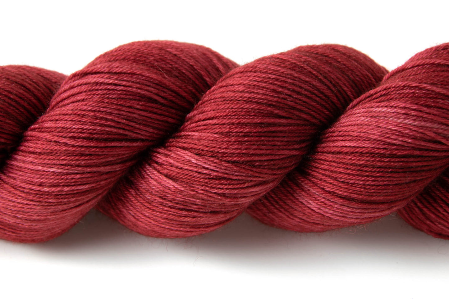 Closeup on the tonal qualities of the yarn: deep red patches with lighter, almost pink highlight throughout.