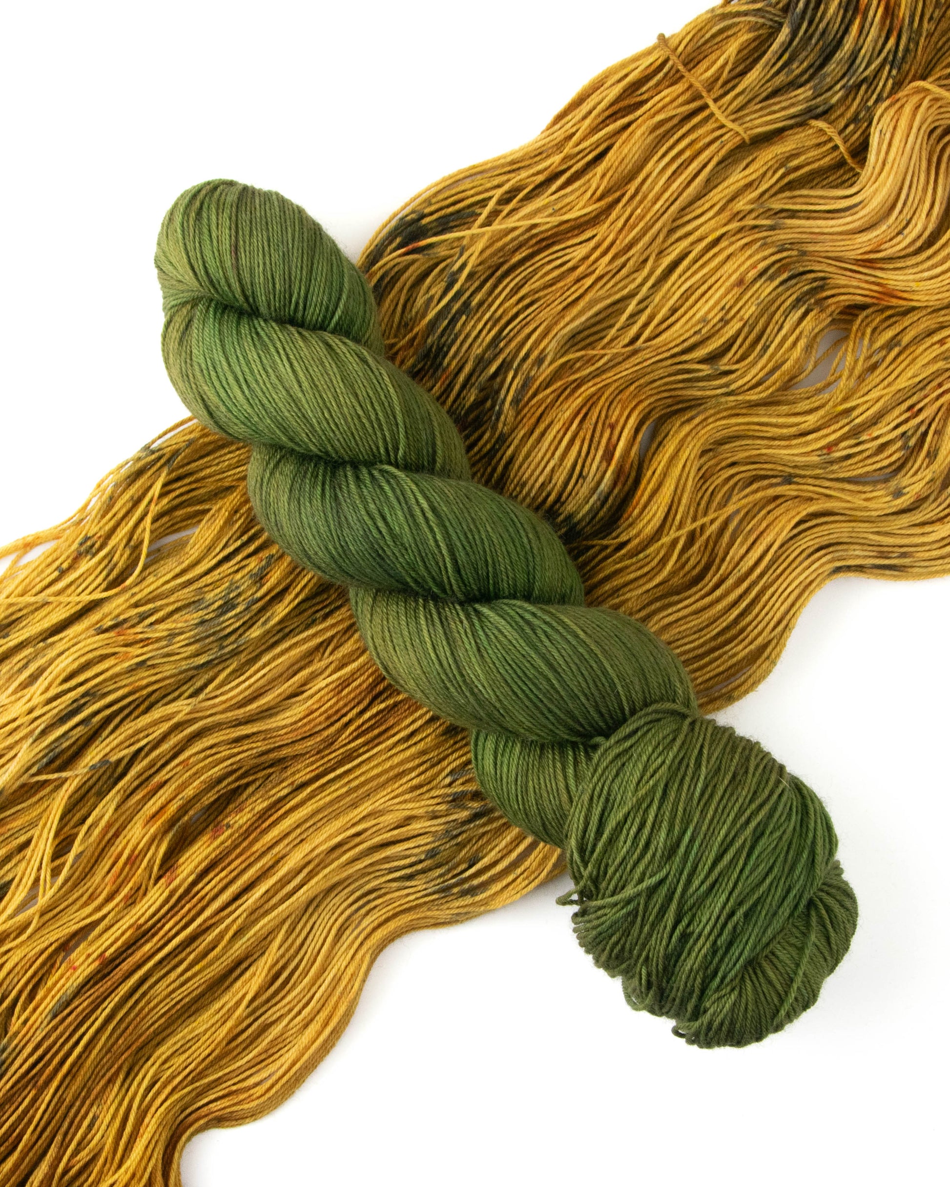 A skein of olive green yarn on top of brown yarn.