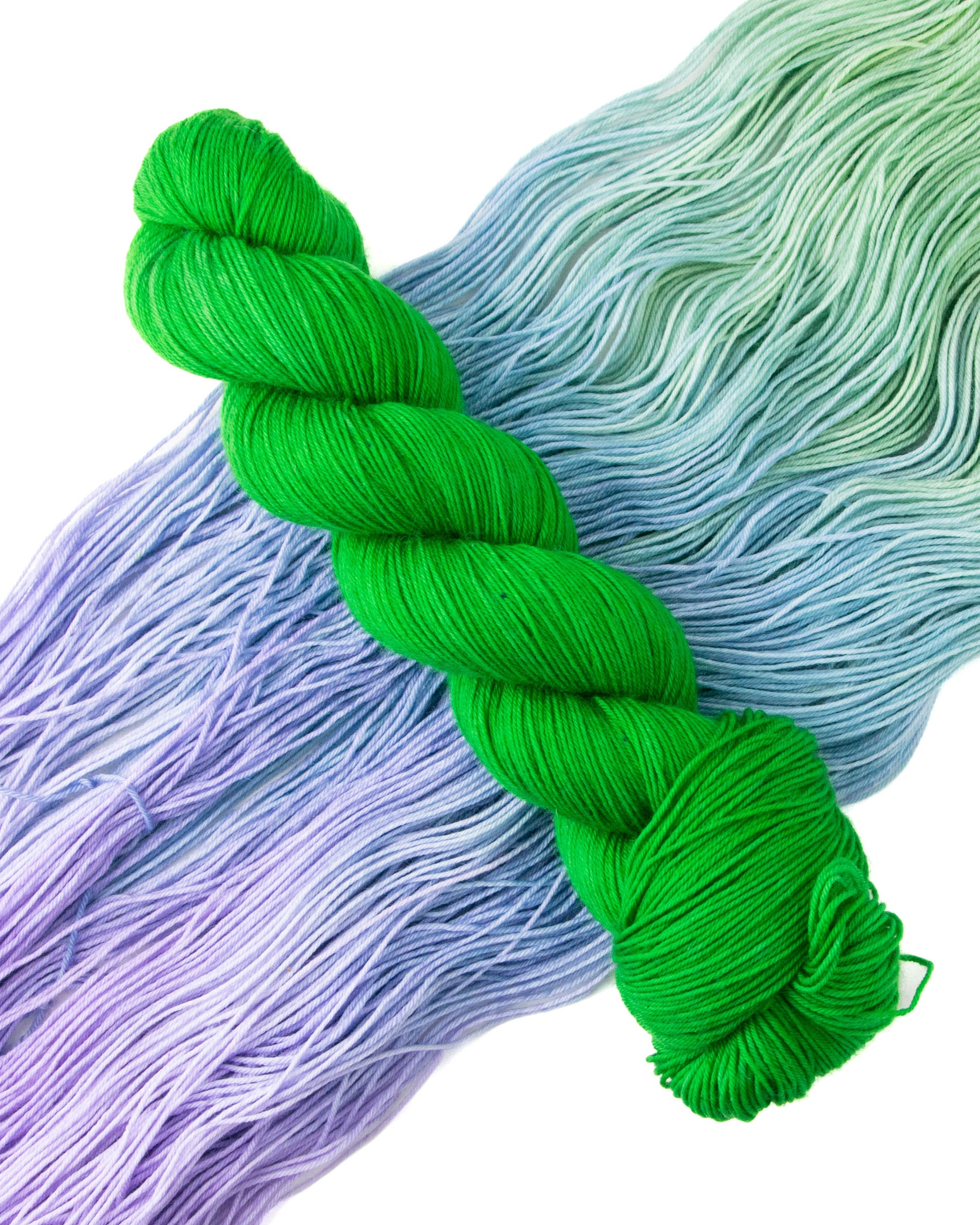 A skein of bright green yarn on top of green, blue, and purple yarn.