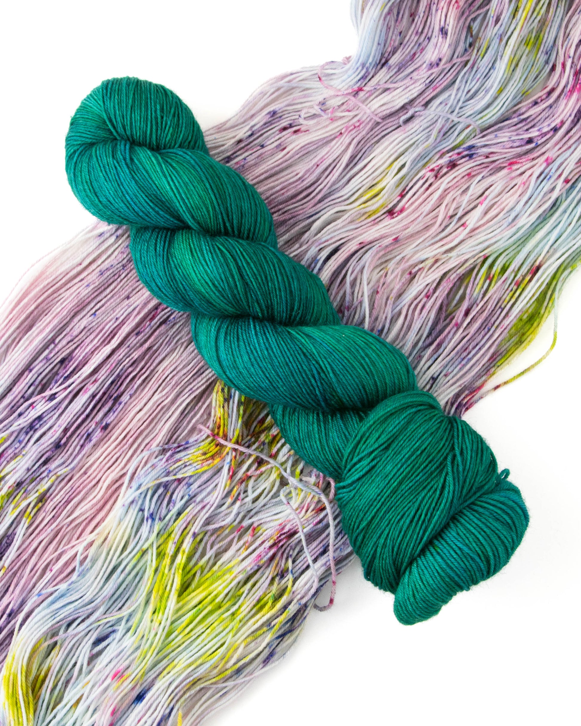 A skein of teal yarn on top of a skein with pink, purple, blue, and green speckles.