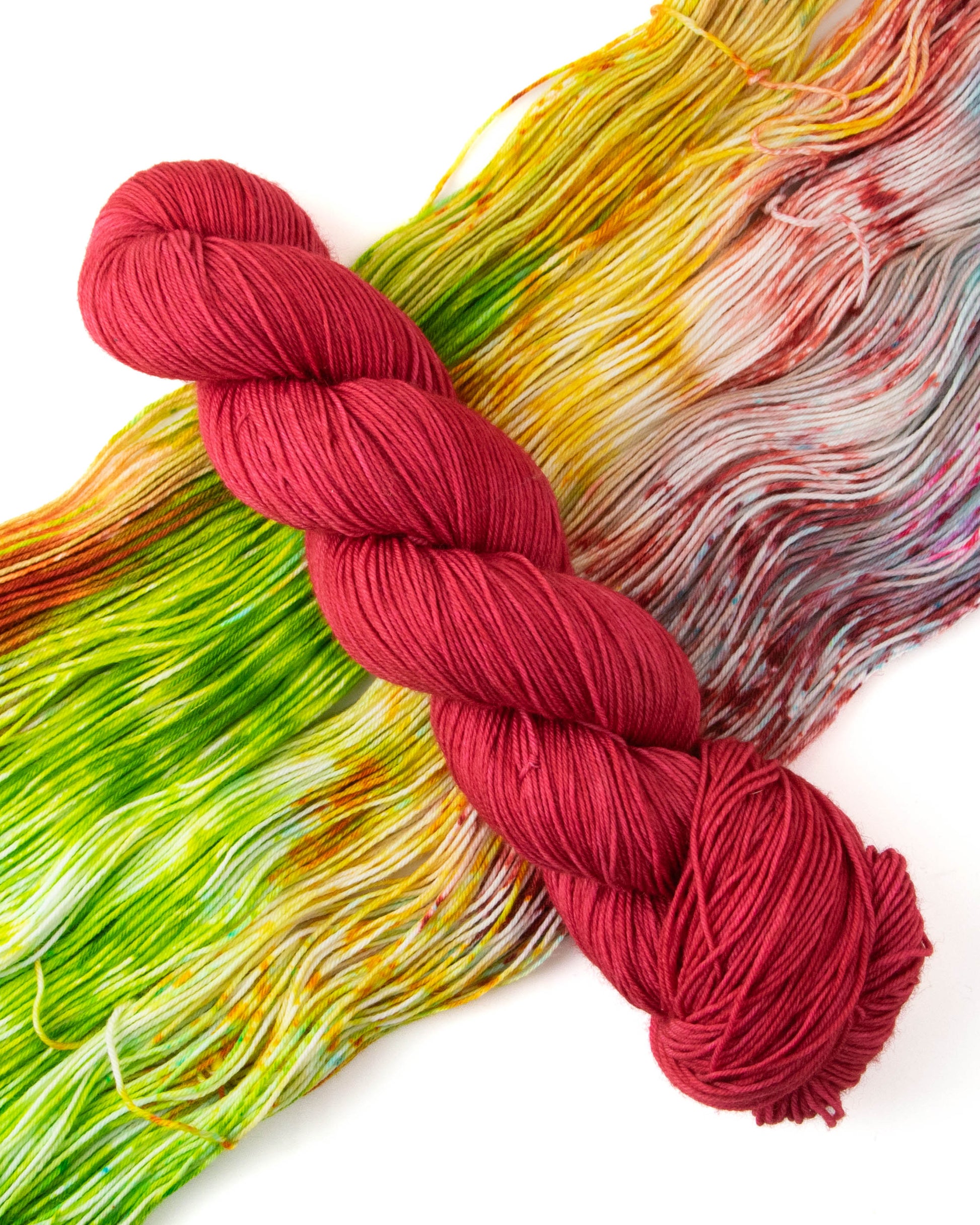 A skein of red yarn on top of rainbow yarn.