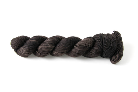 An iron-black skein of hand-dyed tonal yarn, with small patches of lighter gray and brown.