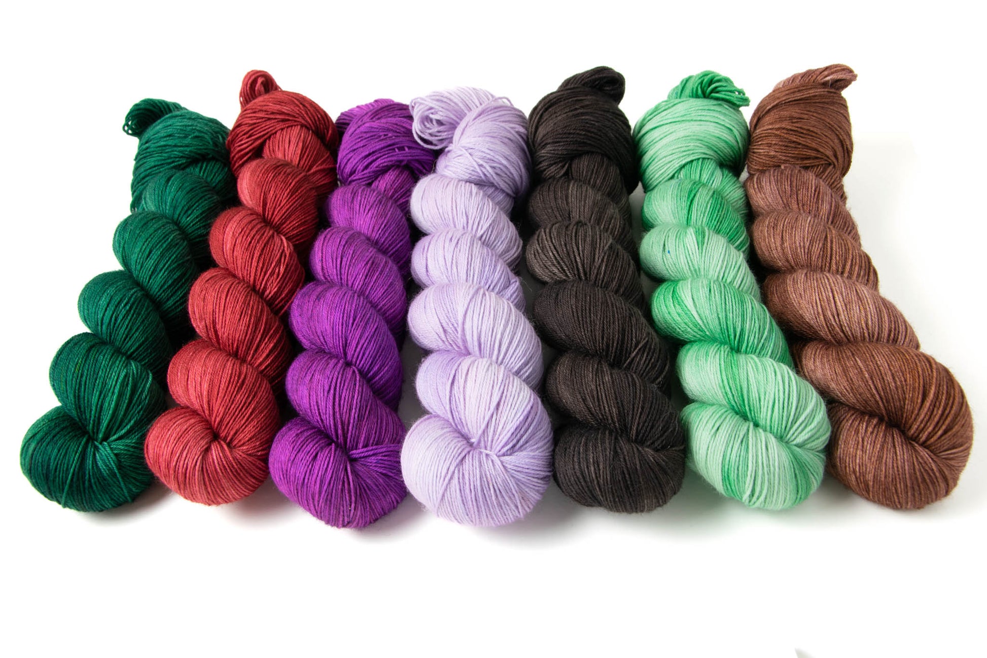 The seven Tonal skeins of the Cabin Collection: dark green, bright red, electric purple, pastel purple, black, pastel green, and brown.