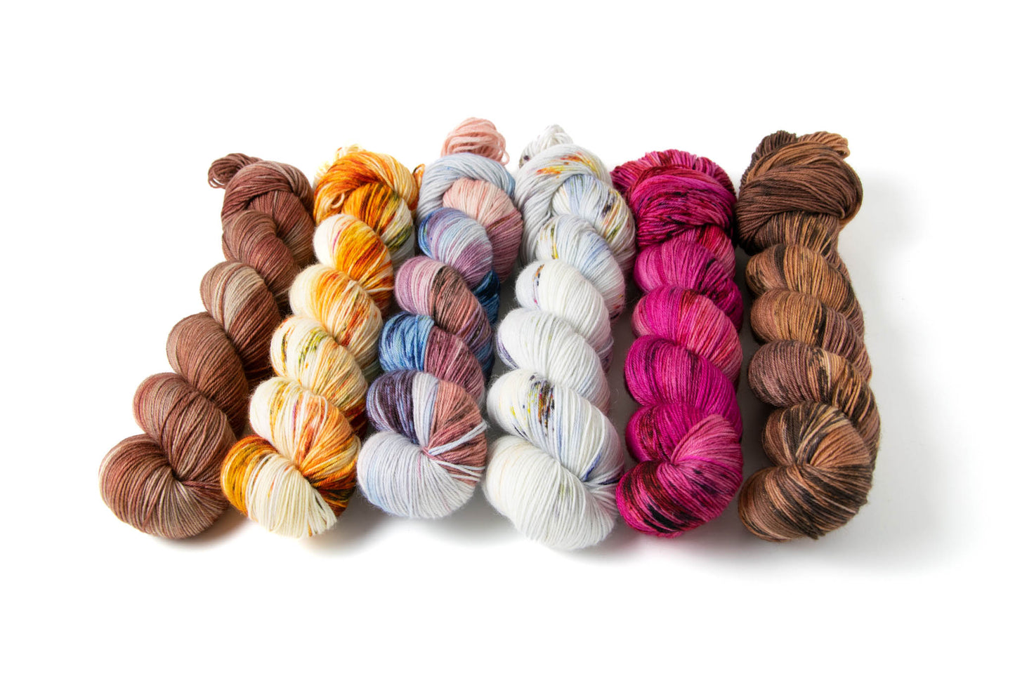 The six variegated skeins in the collection: a dusty tan with brick red accents; a bright red, orange, and green on a white background; a many-shaded blue, mauve, and pink; a bright fuchsia with dark magenta accents; and a warm orange-brown with sections of deeper and cooler browns.