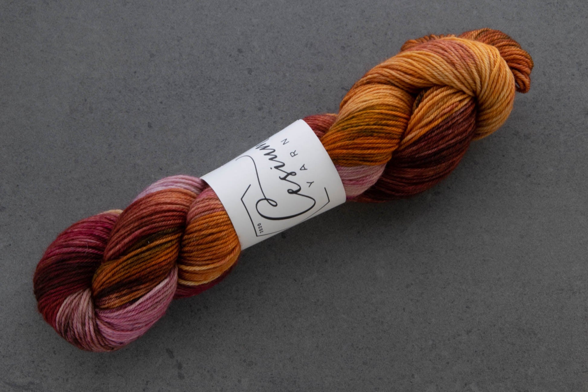 A skein of hand-dyed wool yarn with sections of orange and maroon.