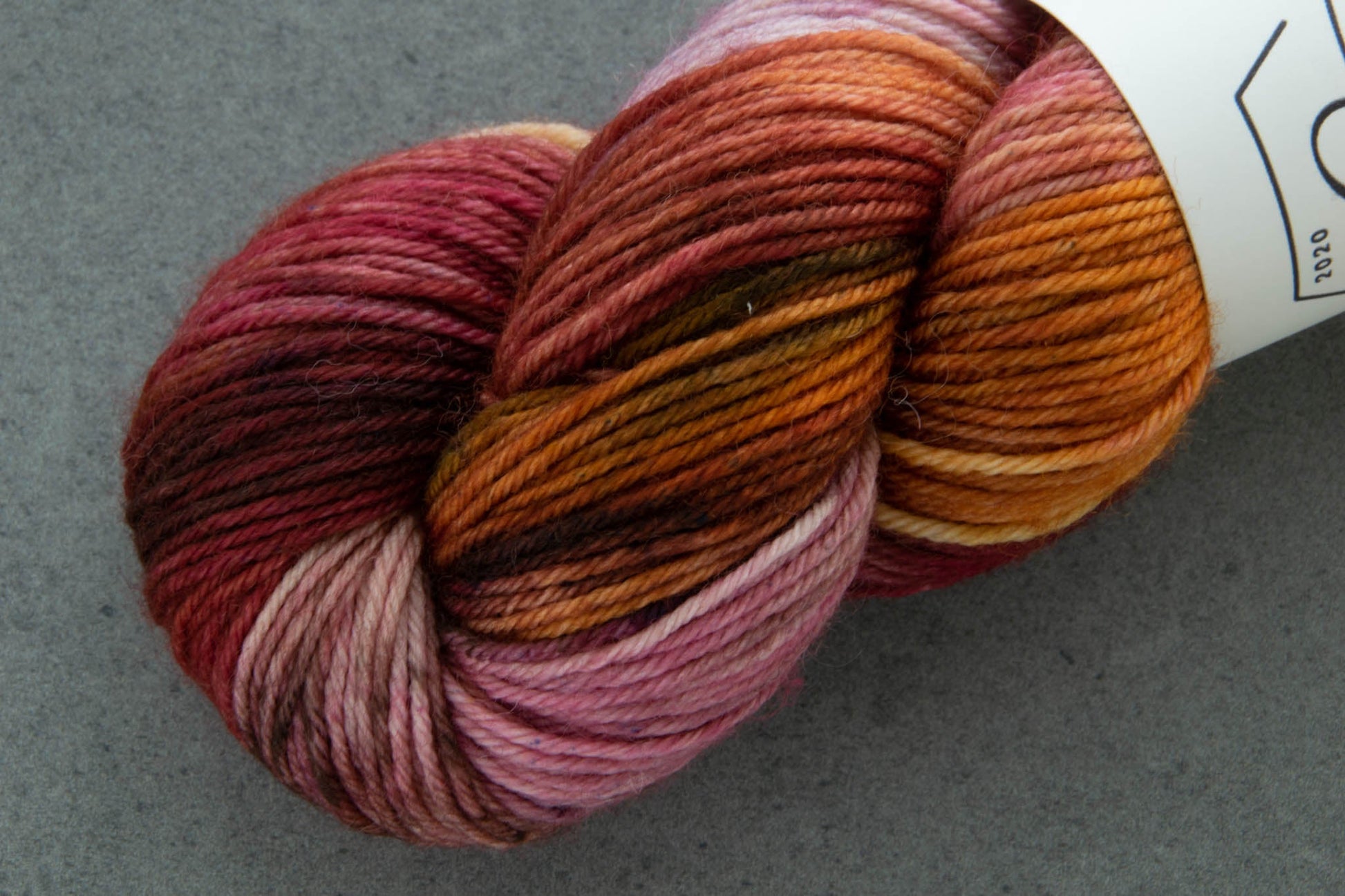 Closeup of one side of the skein with dark maroon, light pink, orange, and coppery brown sections.