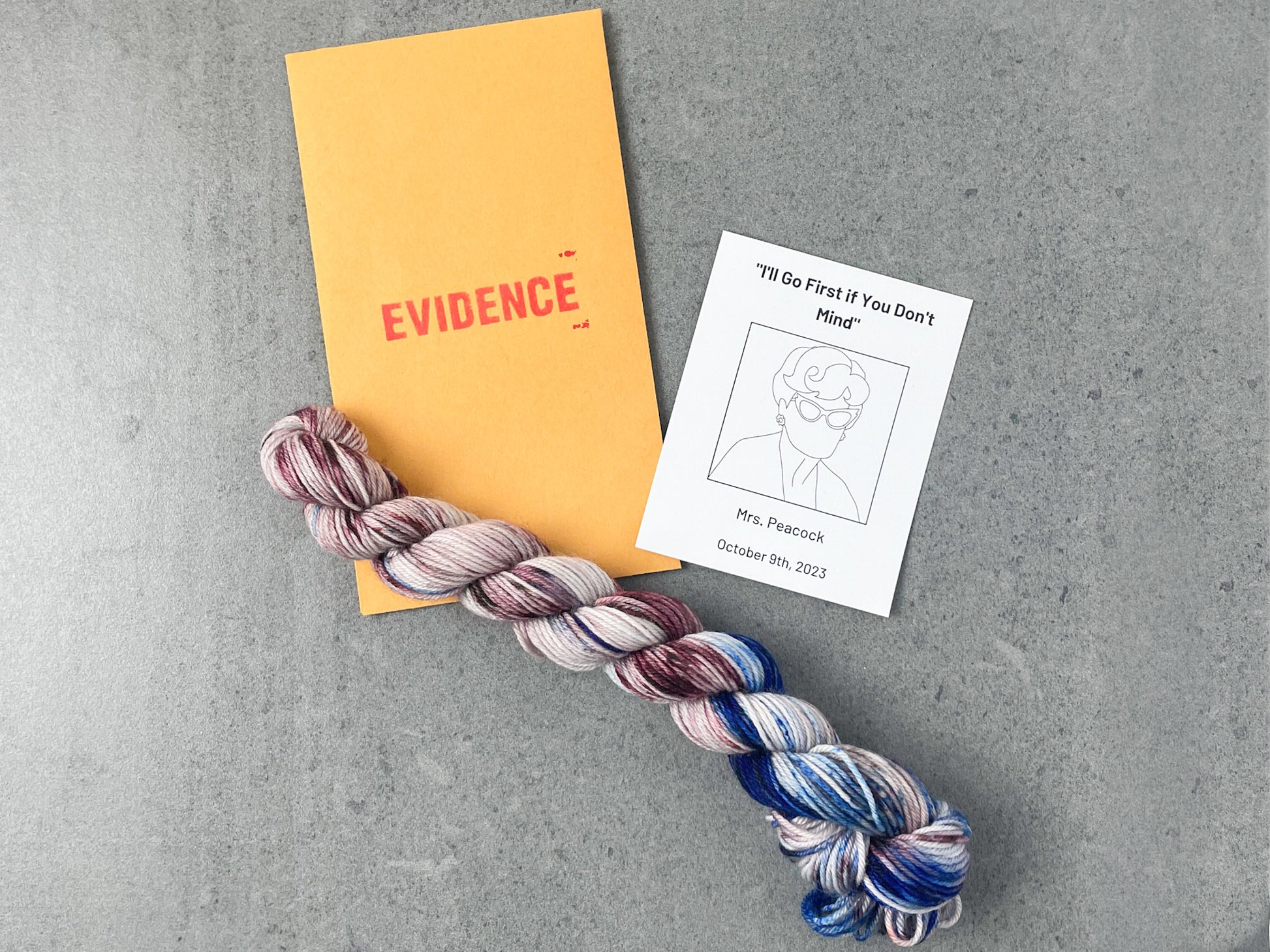 A skein of blue and purple yarn on top of an envelope stamped with "Evidence" and a card with a drawing of Mrs. Peacock on it.