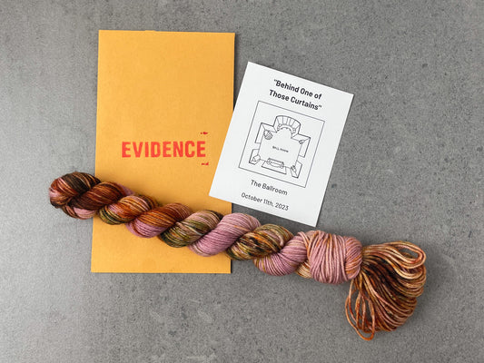 A a pink skein of yarn with large speckles of brown, orange and green on top of an envelope stamped with "Evidence" and a card with an overhead drawing of the ballroom on it.