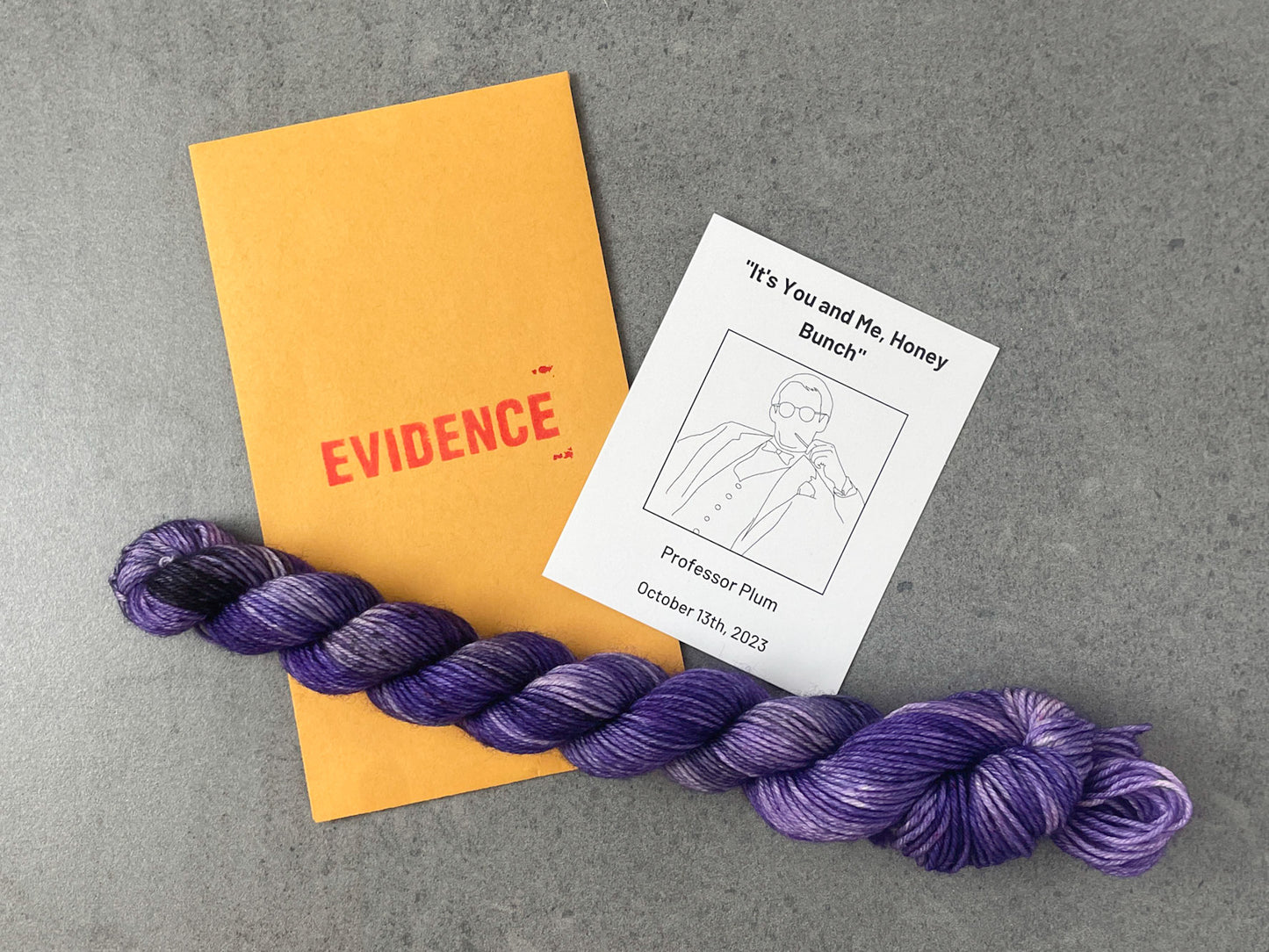 A skein of deep purple yarn on top of an envelope stamped with "Evidence" and a card with a drawing of Professor Plum on it.