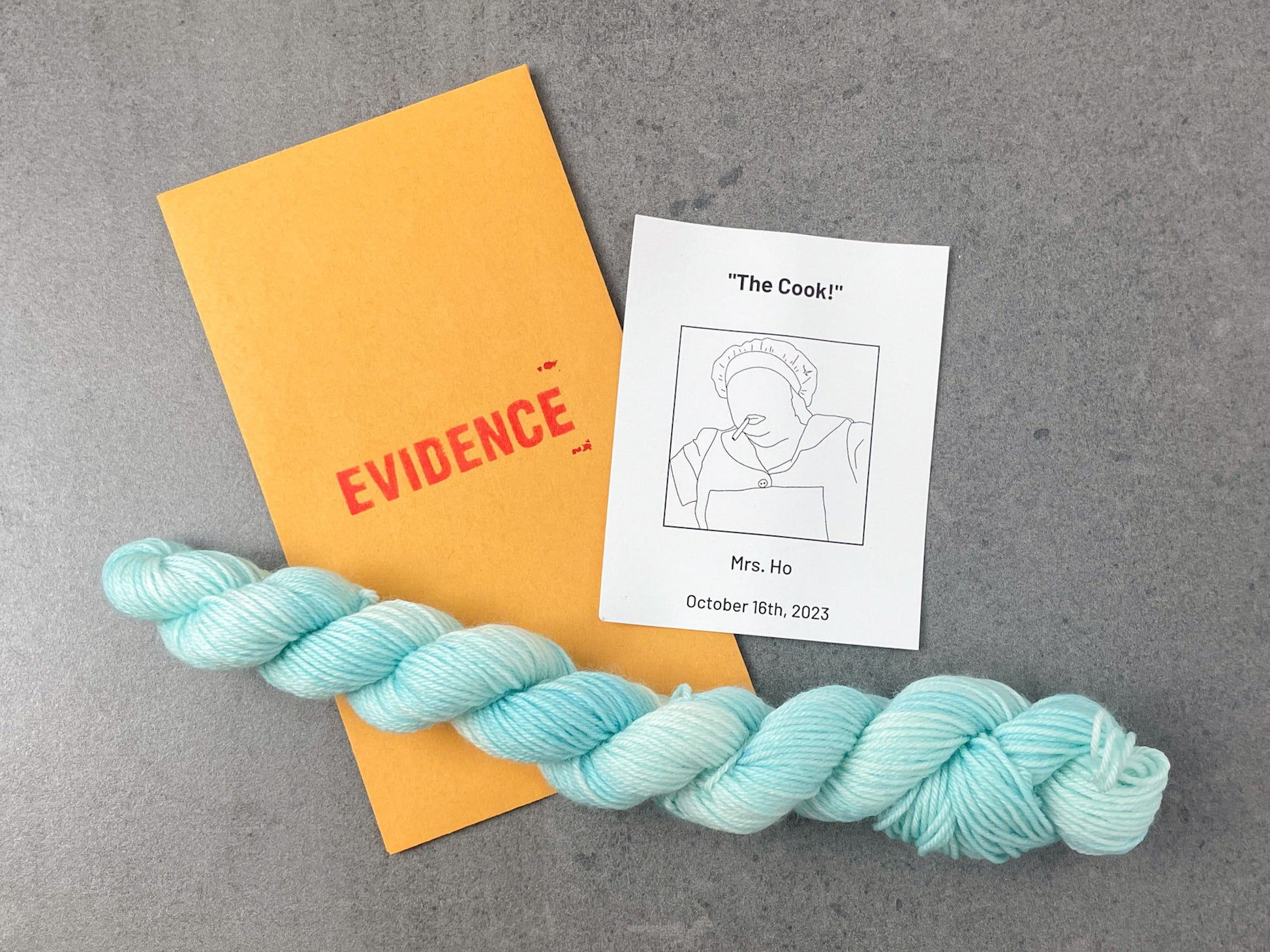 A skein of aqua tonal yarn on top of an envelope stamped with "Evidence" and a card with a drawing of Mrs. Ho on it.