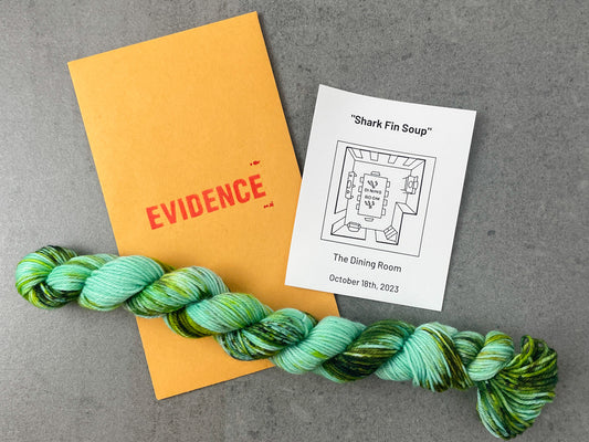 A skein of aqua yarn with bright and dark green speckles on top of an envelope stamped with "Evidence" and a card with an overhead drawing of the dining room on it.
