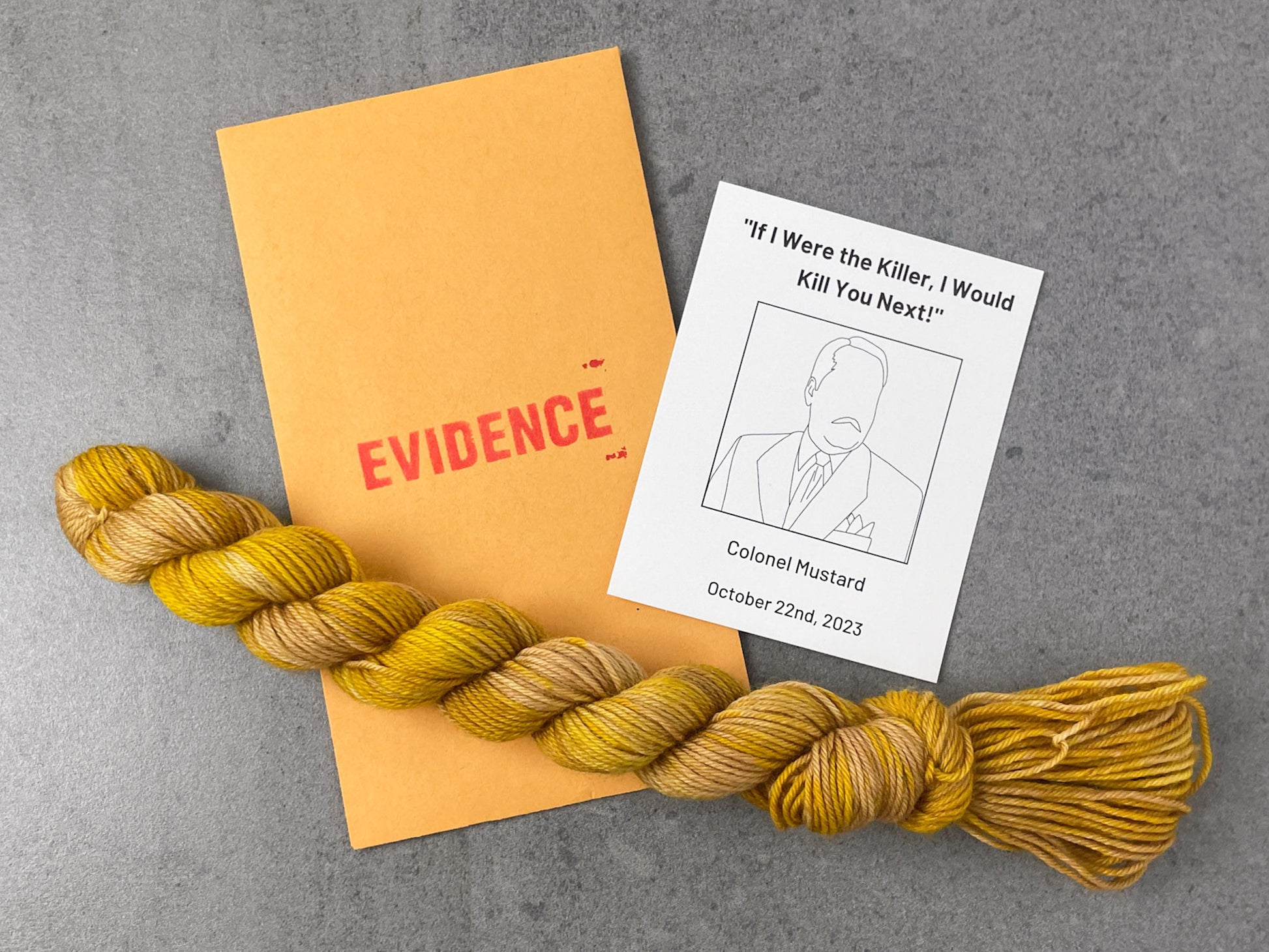 A skein of mustard yellow yarn on top of an envelope stamped with "Evidence" and a card with a drawing of Colonel Mustard on it.