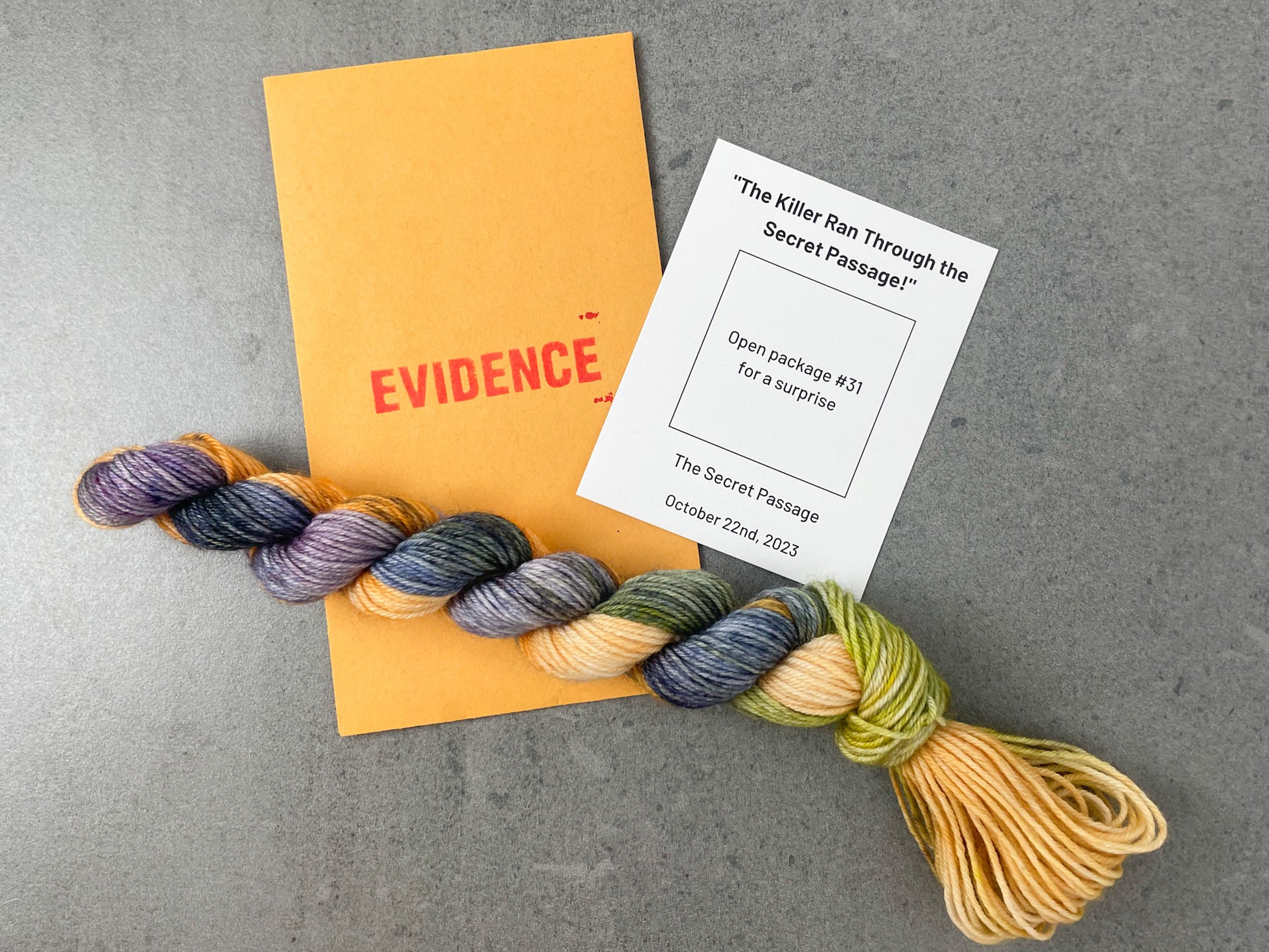 A variegated skein of purple, blue, green, and orange yarn  on top of an envelope stamped with "Evidence" and a white card with colorway information on it.