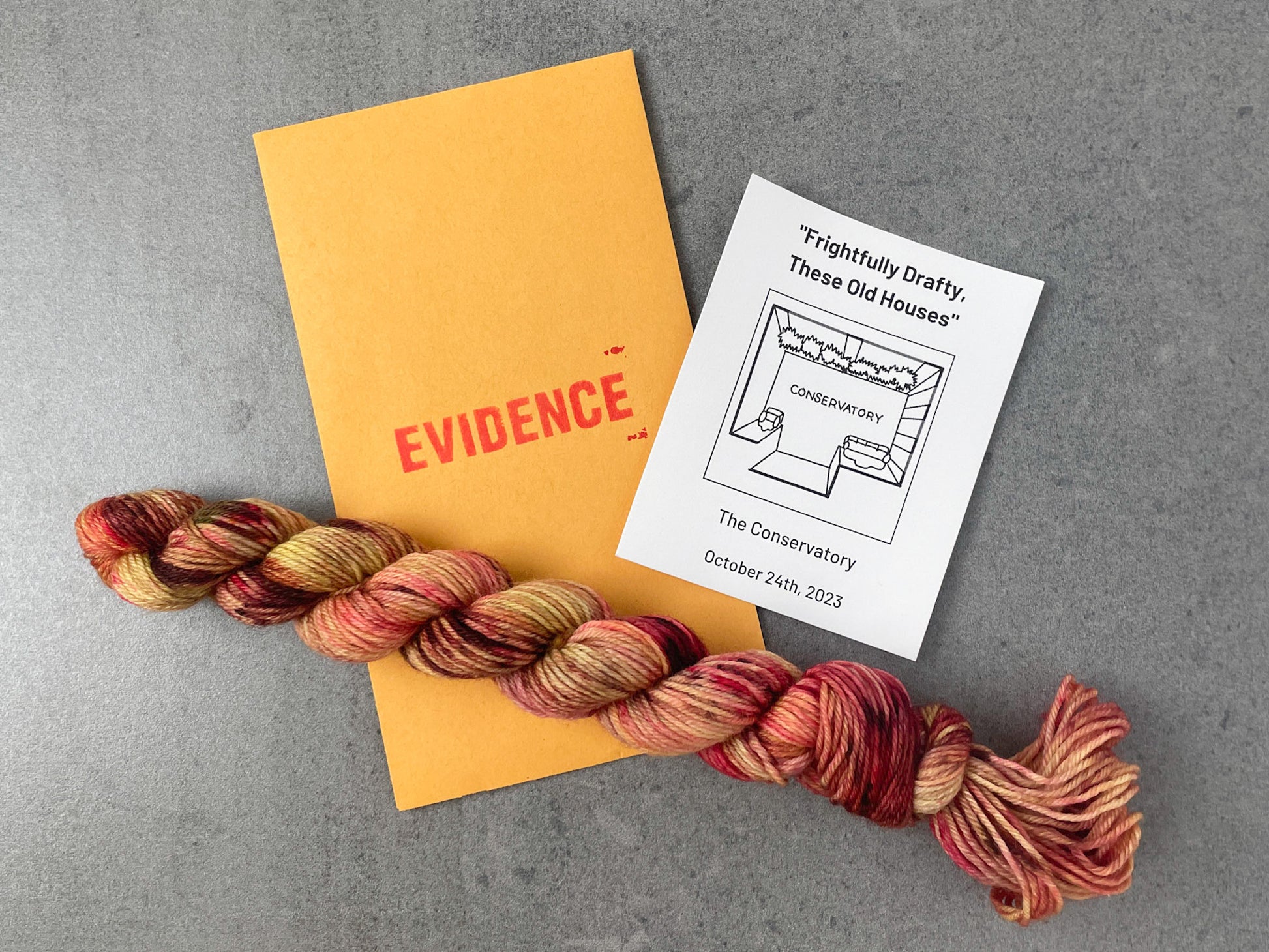 A skein of red, yellow, and pink yarn on top of an envelope stamped with "Evidence" and a card with an overhead drawing of the conservatory on it.