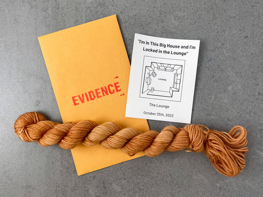 A skein of muted orange tonal yarn on top of an envelope stamped with "Evidence" and a card with an overhead drawing of the lounge on it.