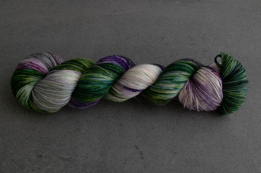 A skein of green, purple, and white variegated hand-dyed wool yarn.