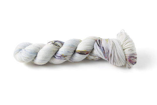 A white skein of yarn with many colors of dark speckles.