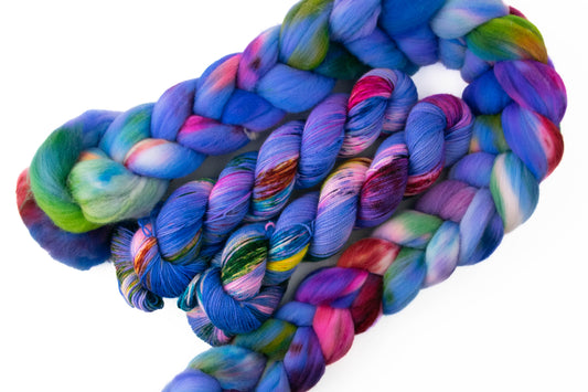 A coiled bundle of variegated yarn and fiber in vivid shades of blue, purple, pink, green, and orange on a plain white background.