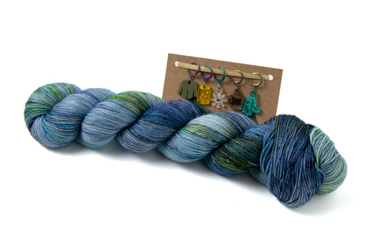 A skein of blue yarn with green sections and a set of five stitch markers on a card.