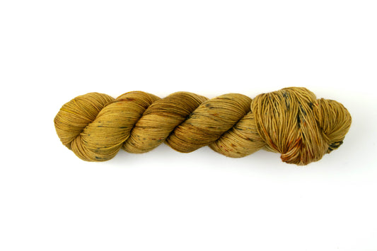 A skein of golden ochre yarn with brown, black, and occasional burnt orange speckles.