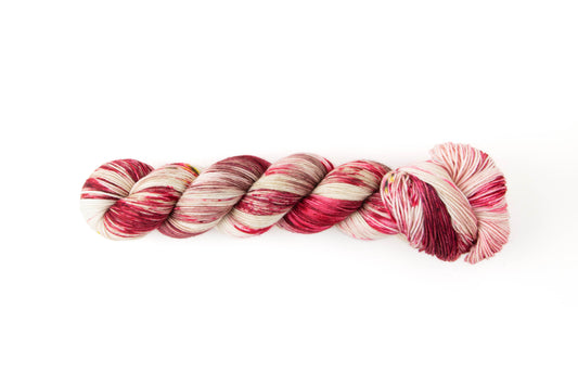 A skein of white yarn with large sections of red and mauve and small patches of yellow.