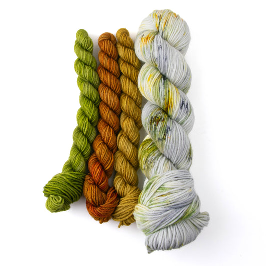 Three mini skeins in green, orange, and yellow, next to a variegated full skein with patches of yellow, green, and gray on a white background.