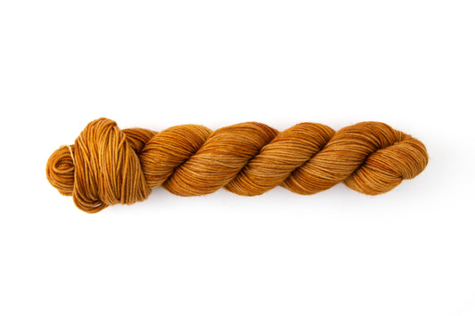 A tan-toned orange skein of hand-dyed wool yarn.