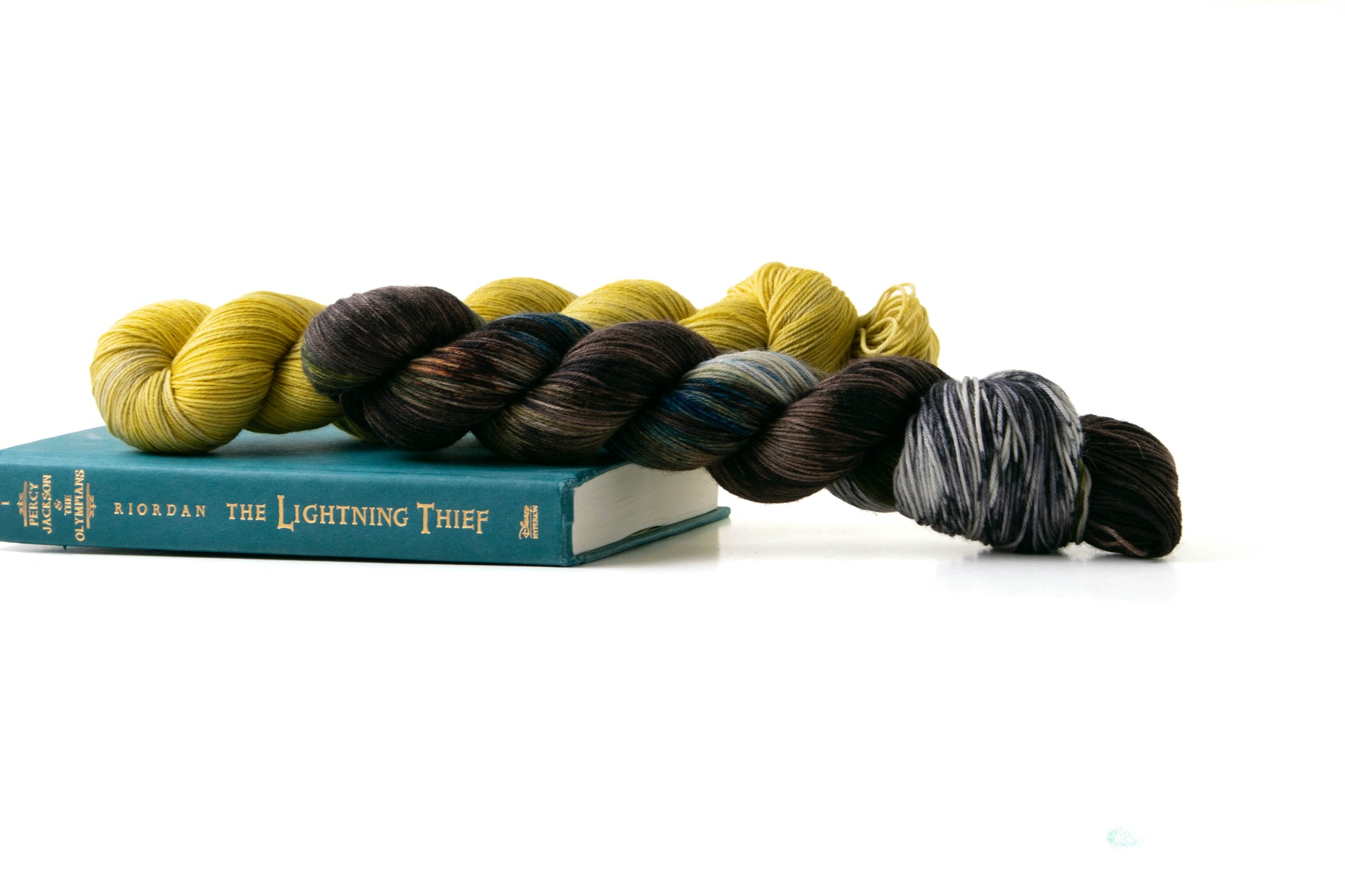 Two skeins of yarn, one variegated and one tonal, sitting on a well-loved copy of The Lightning Thief.